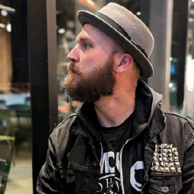 Profile portrait of Matthew Huntsberry wearing a gray brimmed hat and a dark jacket indoors.”